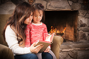 mother reading to child next to fireplace
